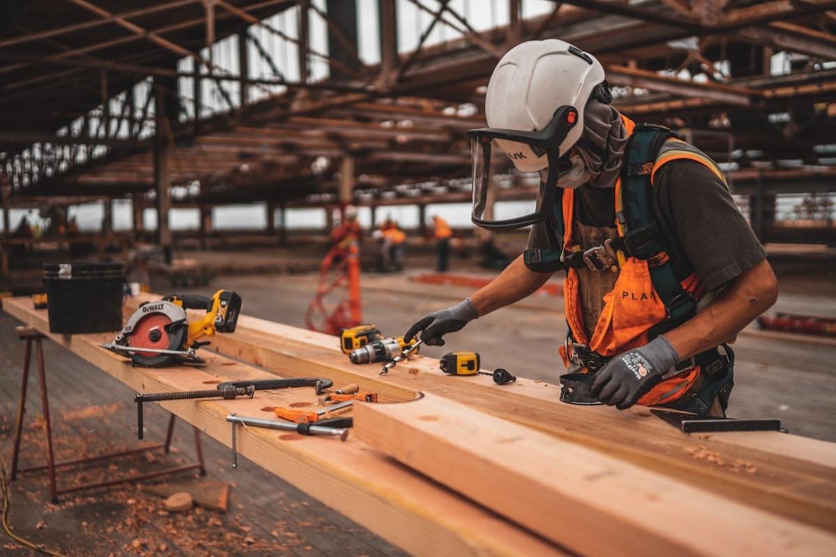 A builder measuring and cutting a length of framing timber on a worksite.