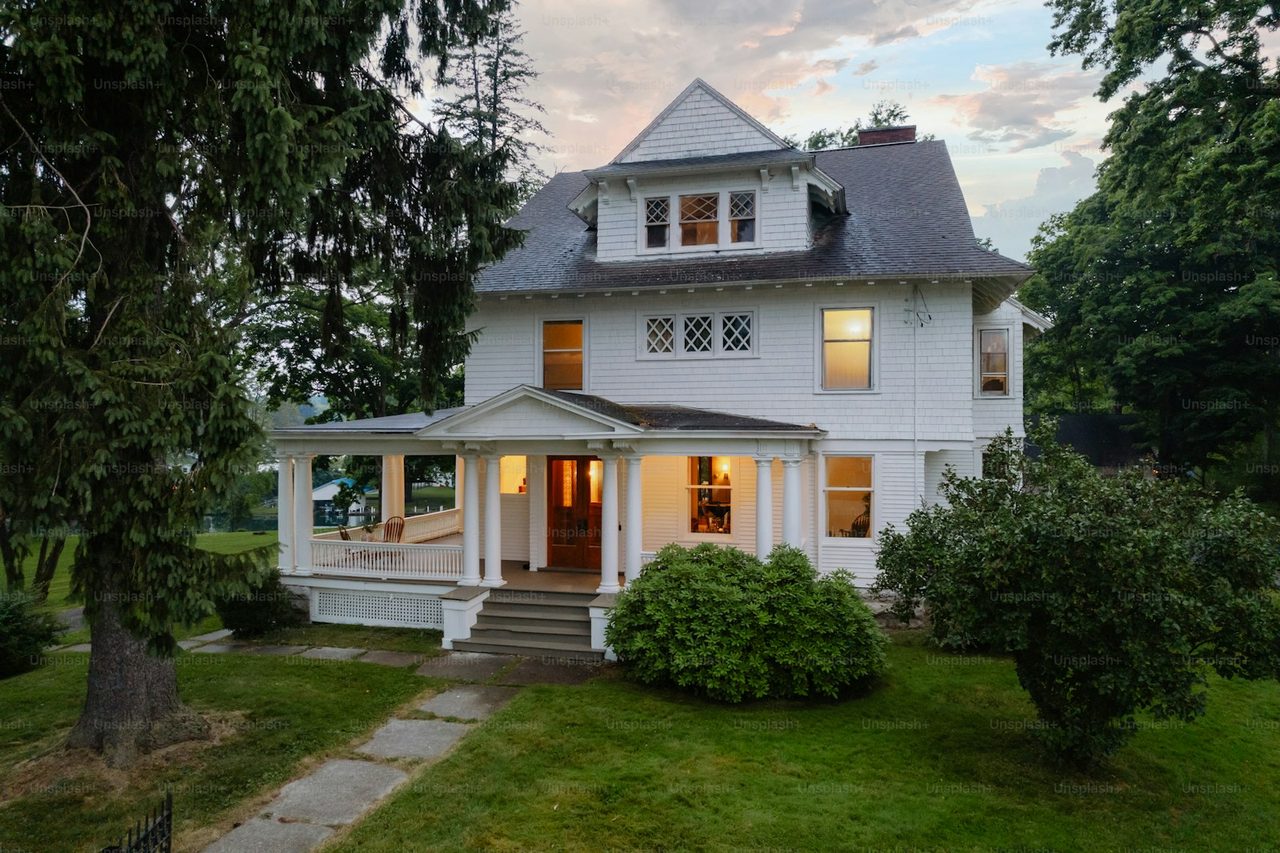 A weatherboard house at dusk with its porch light and windows lit.